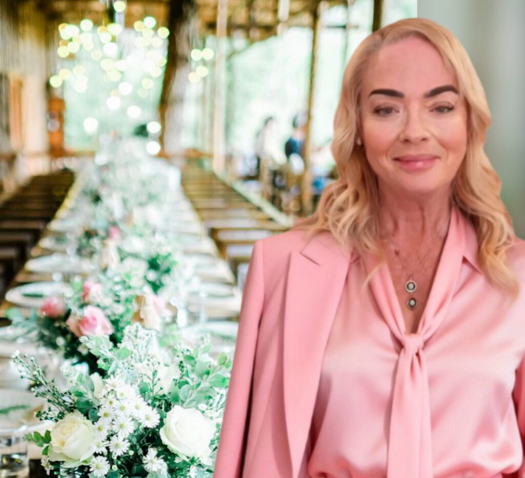 Sandy Kamper in a pink suit beside a decorated Menopause High Tea table